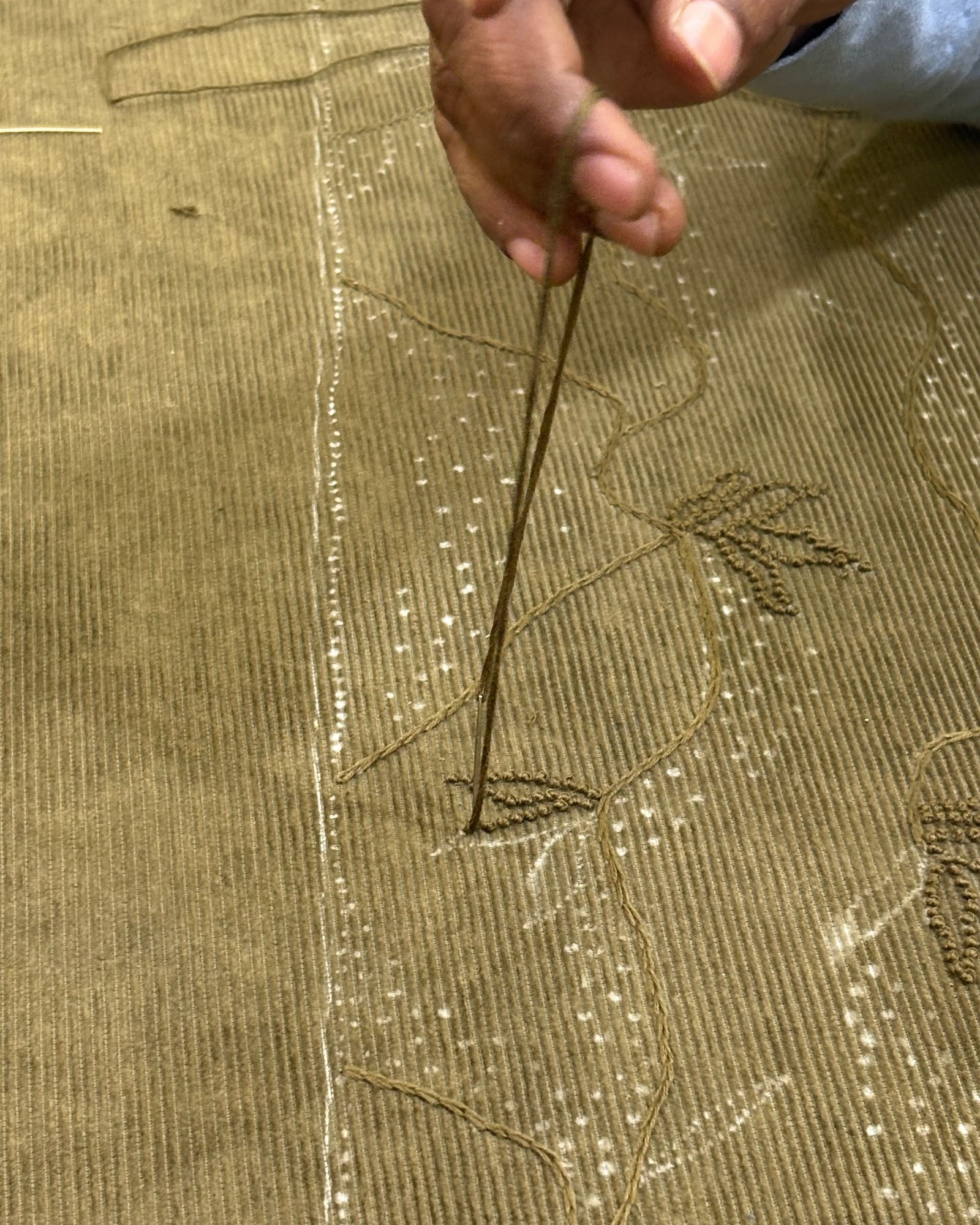 Hand holding a needle over embroidered fabric with a palm tree design.