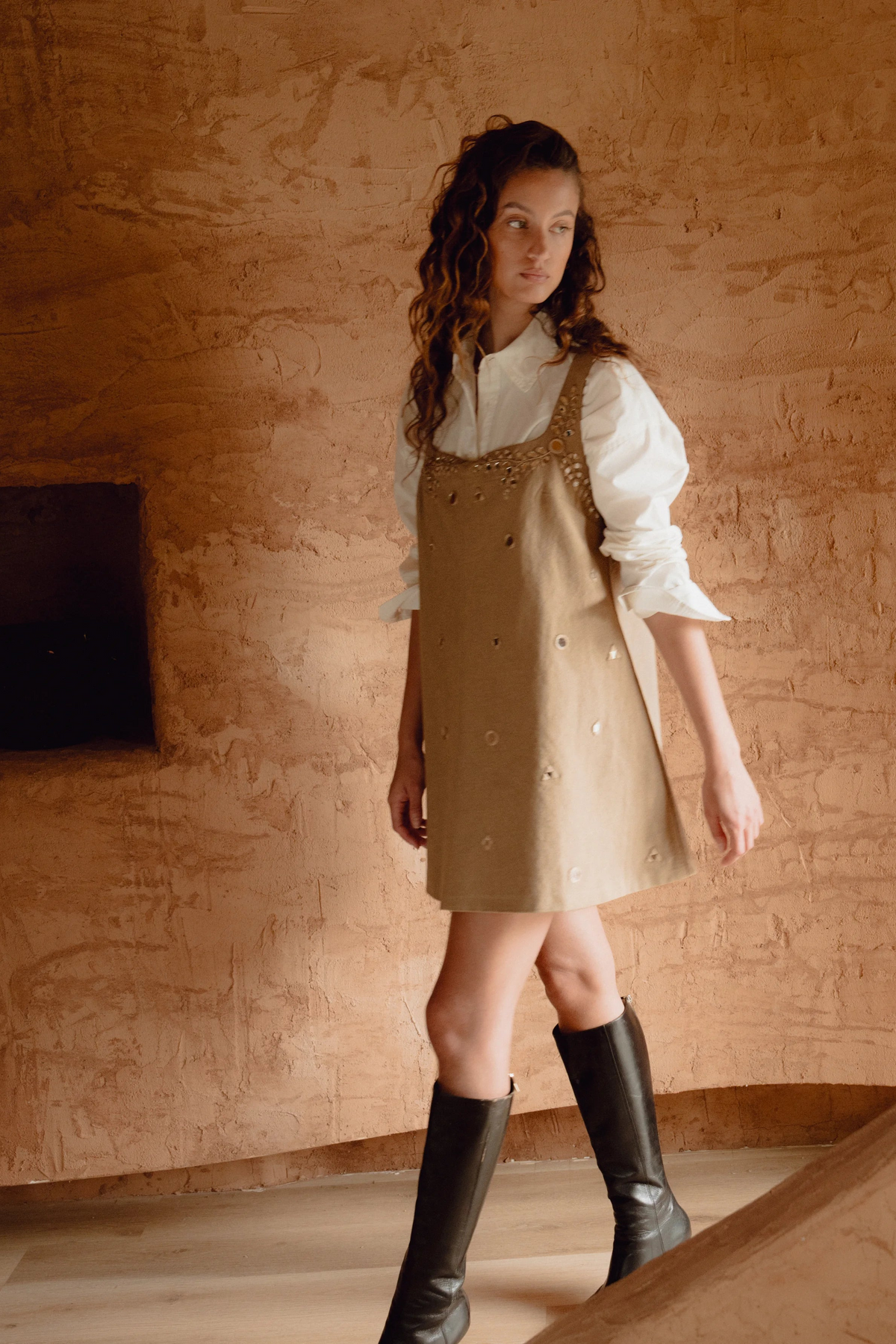 Woman in a beige dress standing in a room with textured walls.